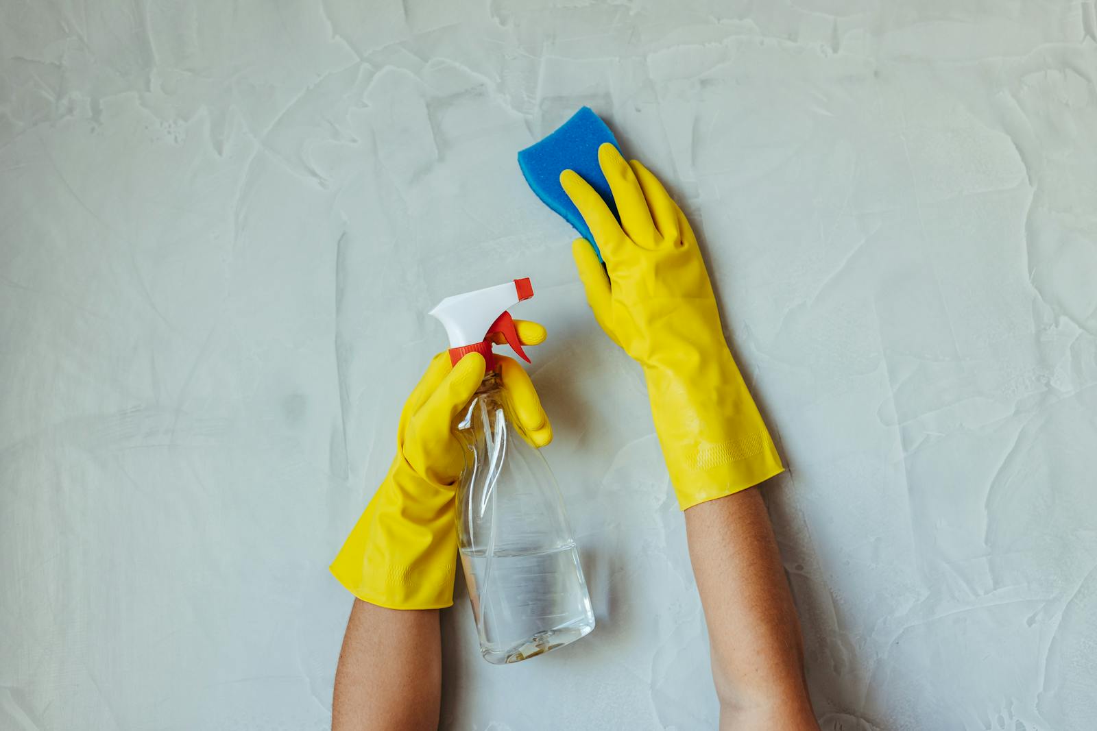 Yellow gloves cleaning a wall with blue sponge